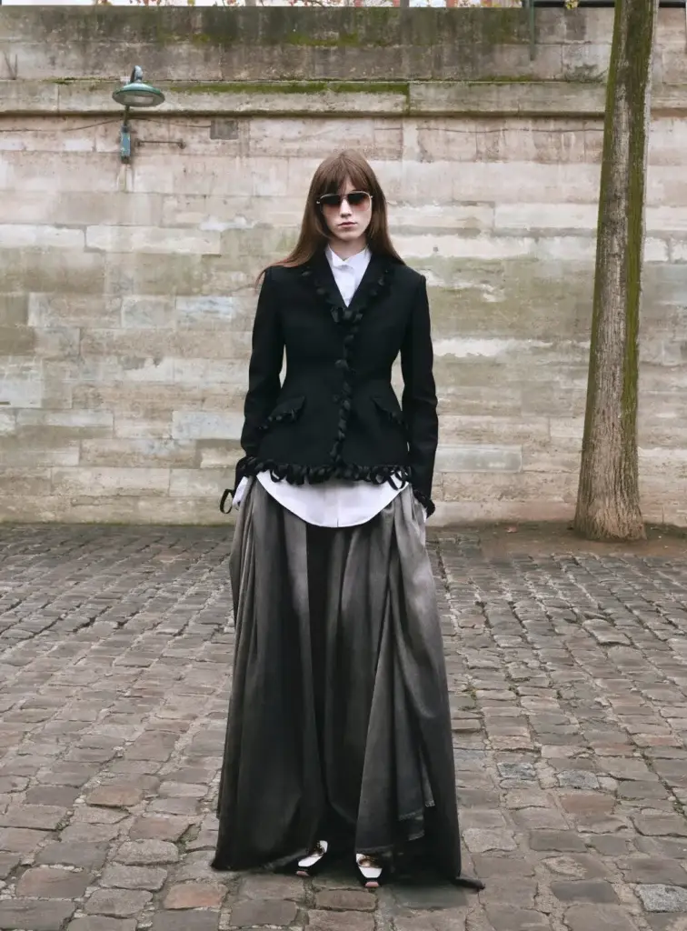 Modelo vestindo look da coleção Dior Pre-Fall 2026 criada por Jonathan Anderson, destacando a reinvenção da silhueta clássica e acessórios modernos.